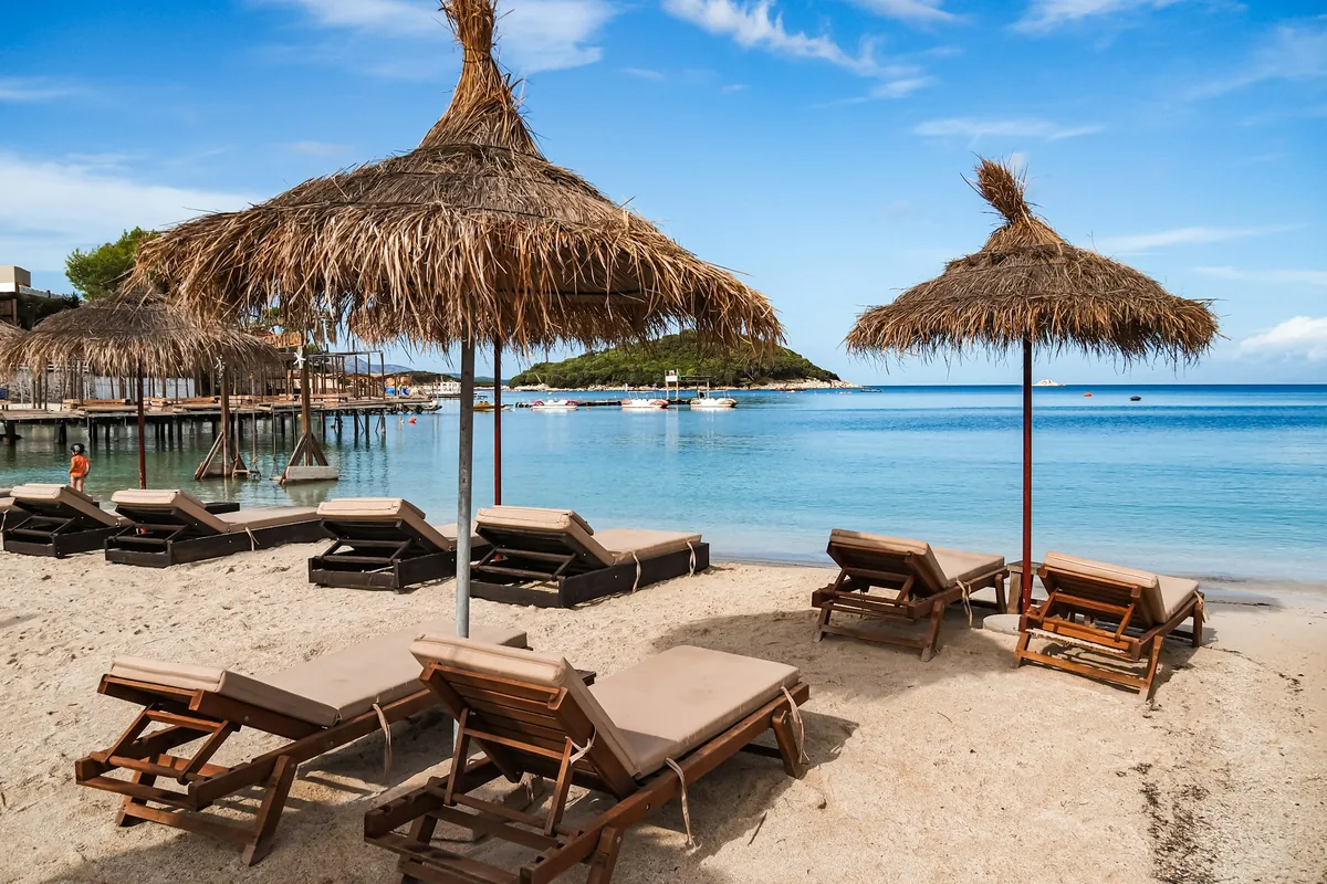 Thatched umbrellas and sunbeds on a beach in Ksamil with small islands offshore