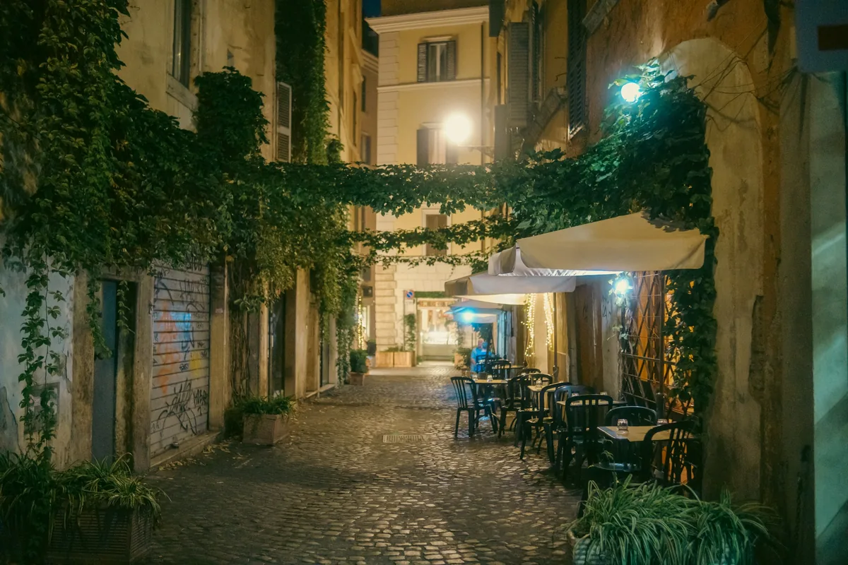 Ivy-covered lane with restaurant tables at night in Trastevere, Rome