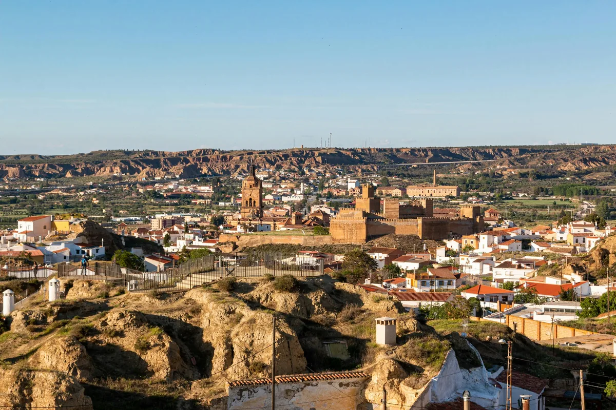 Guadix cathedral and Alcazaba seen across the cave quarter, with cave chimneys in front