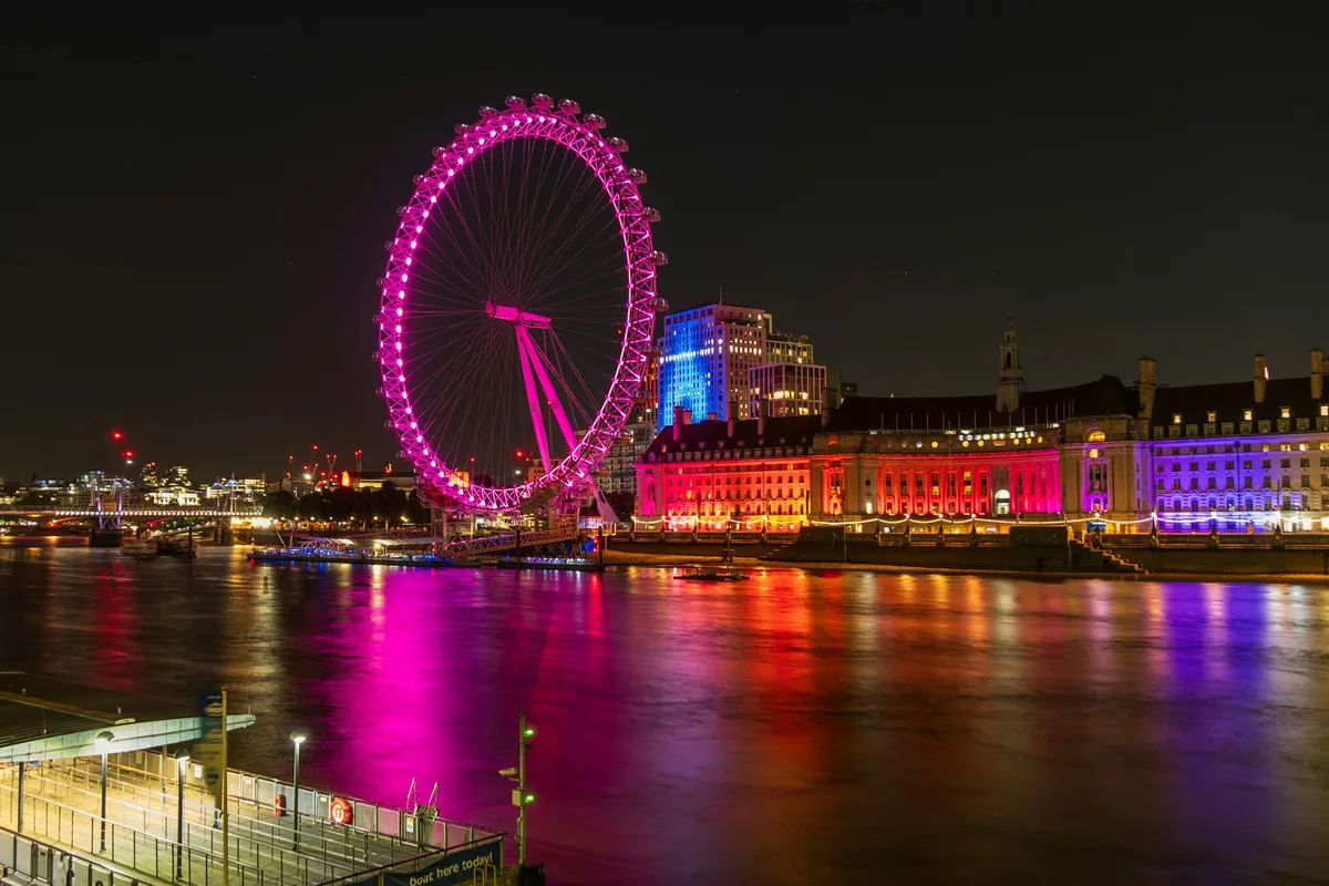 London Eye lit in pink beside the Thames at night