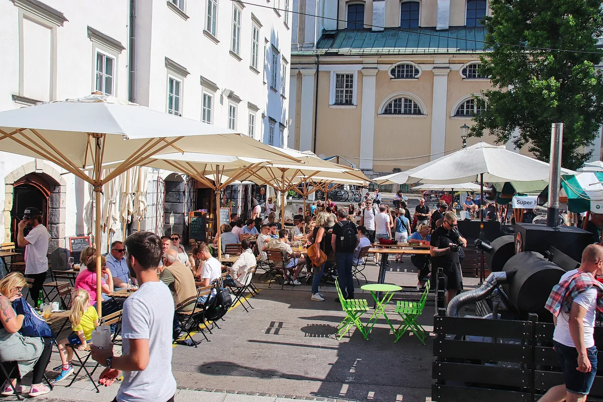 Diners at tables under parasols at the Odprta Kuhna Friday food market in Ljubljana