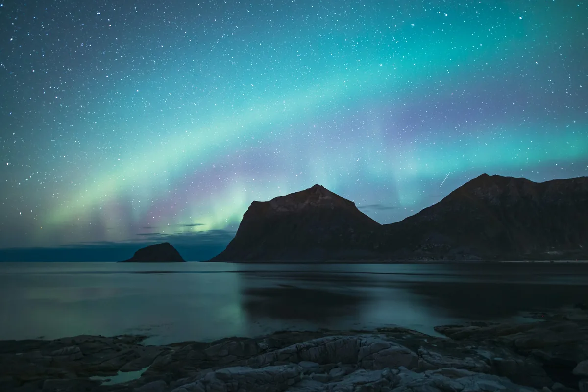 Green and purple aurora over dark mountains and still water