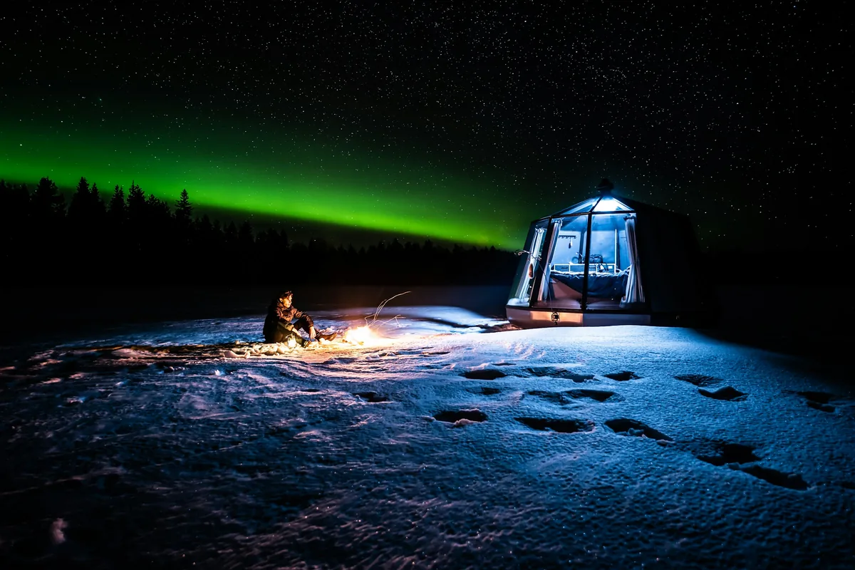 Glass igloo under green Northern Lights in Finnish Lapland