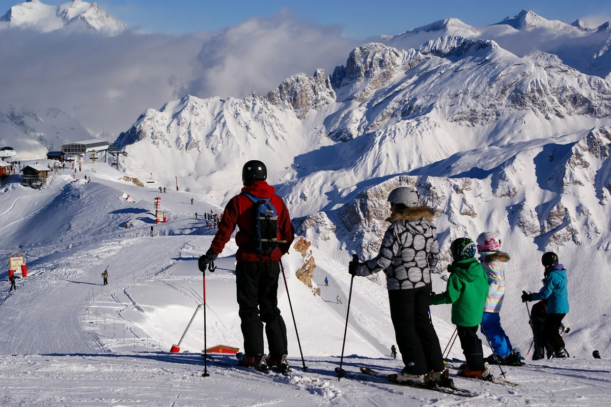 A family on skis at the top of a gentle slope in the Alps