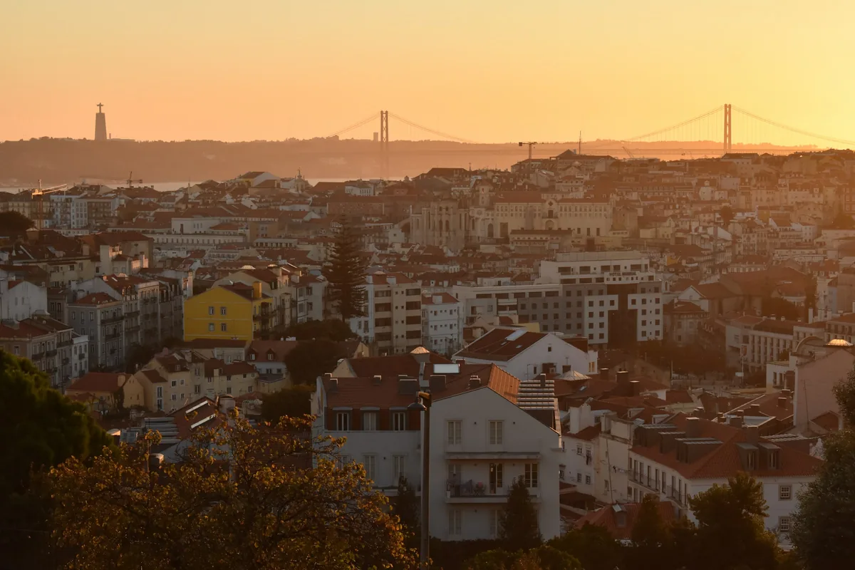 Golden hour over Lisbon's rooftops with the 25 de Abril Bridge in the distance