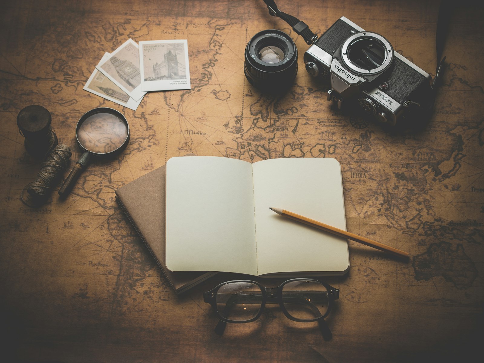 Notebook, pencil, camera and magnifying glass on an old map, ready for trip planning